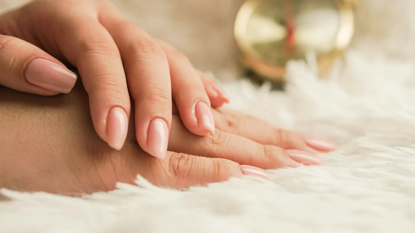 Mãos com unhas em tom nude sobre tecido felpudo claro