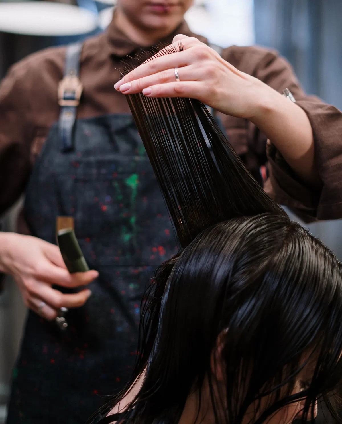 Mãos de profissional penteando mechas de cabelo longo, escuro e liso durante o atendimento
